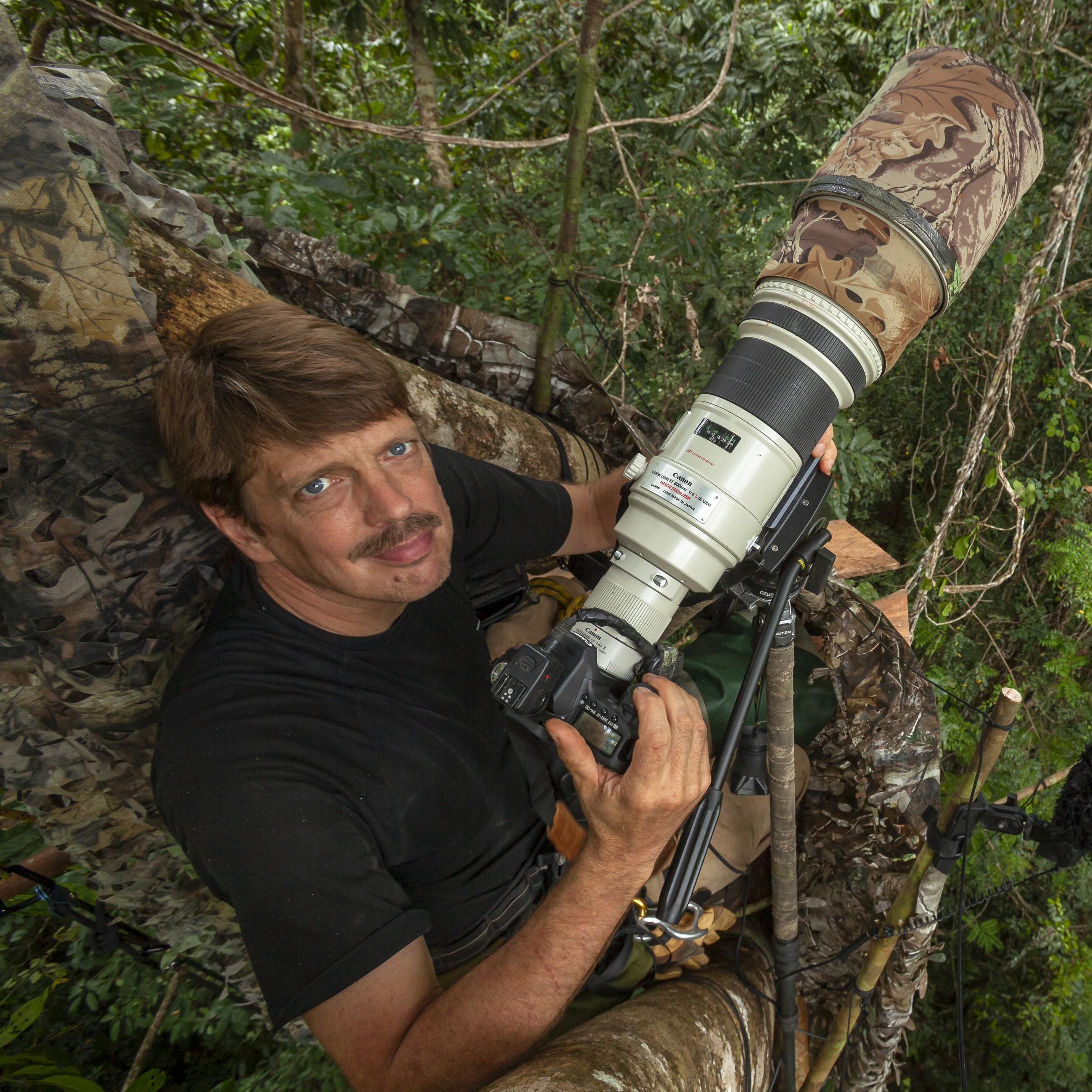 Tim Laman crouched in a rainforest canopy hide behind a large telephoto lens